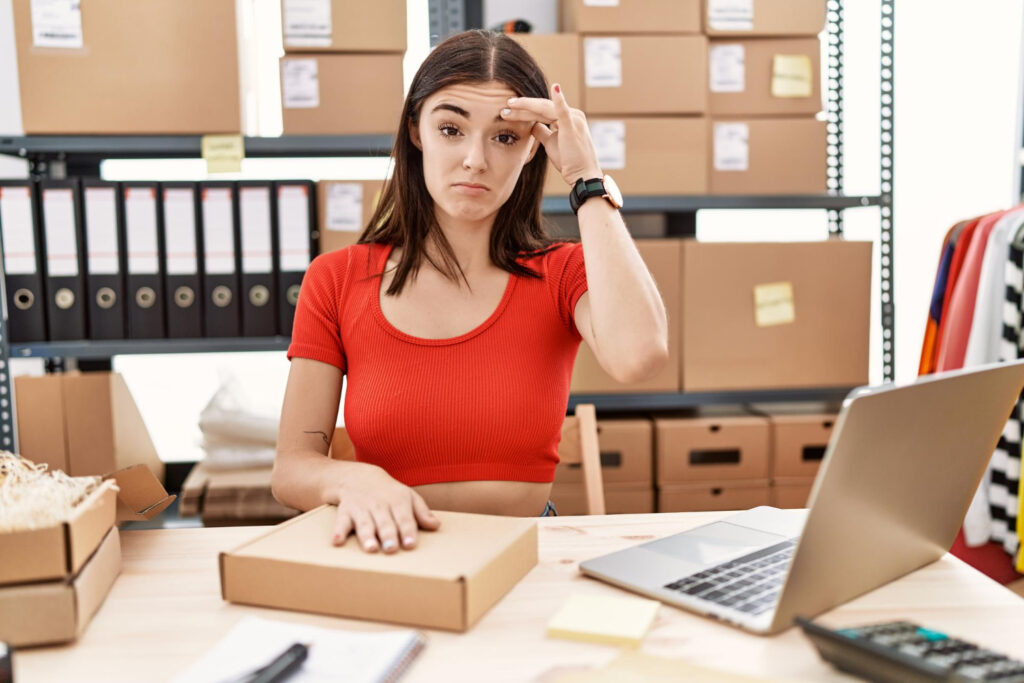 amazon seller tools cost - a woman looking stressed at a desk with boxes and a laptop